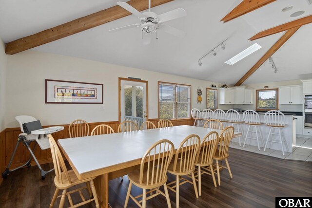 dining room featuring lofted ceiling with skylight, a wealth of natural light, a wainscoted wall, and dark wood-style floors