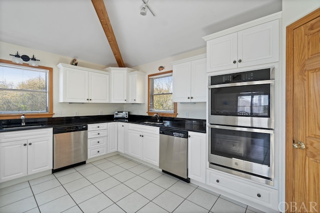 kitchen featuring appliances with stainless steel finishes, dark countertops, a sink, and white cabinetry