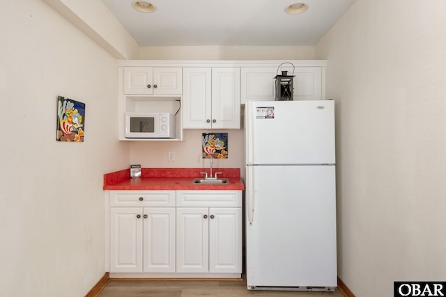 kitchen featuring white appliances, white cabinetry, a sink, and baseboards