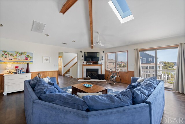 living area with vaulted ceiling with skylight, visible vents, wainscoting, dark wood-style flooring, and a fireplace