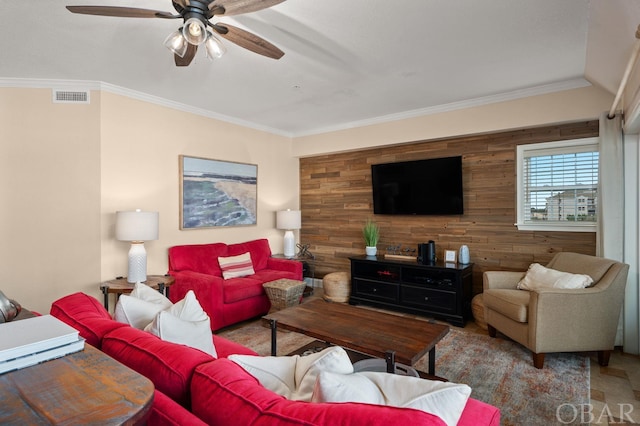 living area with an accent wall, visible vents, a ceiling fan, and ornamental molding