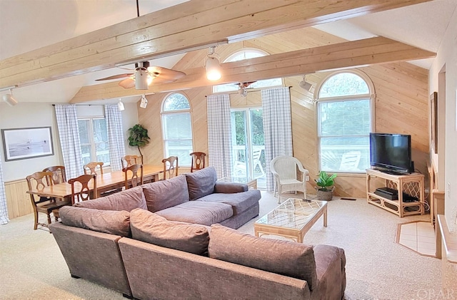 living area featuring vaulted ceiling with beams, wood walls, carpet, and a ceiling fan