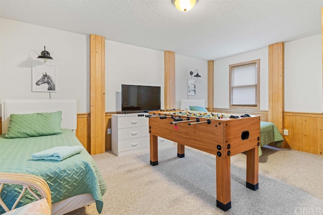 recreation room featuring a textured ceiling, wooden walls, wainscoting, and light colored carpet