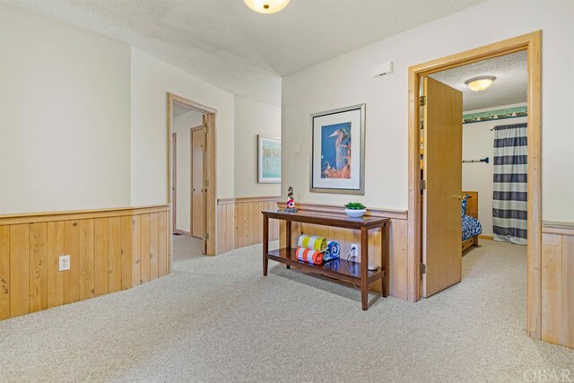 corridor with a wainscoted wall, wood walls, a textured ceiling, and light carpet