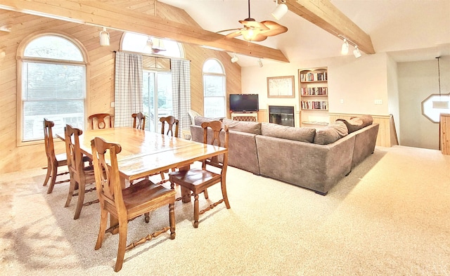 carpeted dining room featuring track lighting, ceiling fan, wooden walls, and lofted ceiling with beams