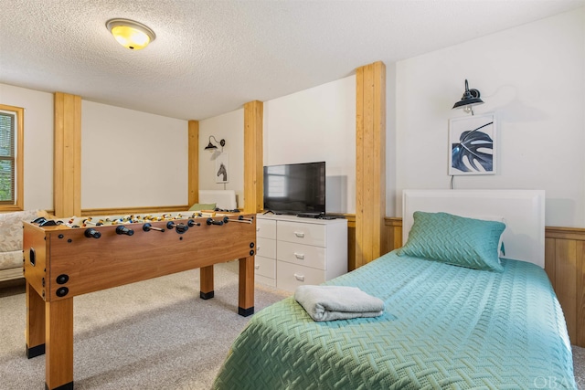 bedroom with wainscoting, a textured ceiling, and light colored carpet