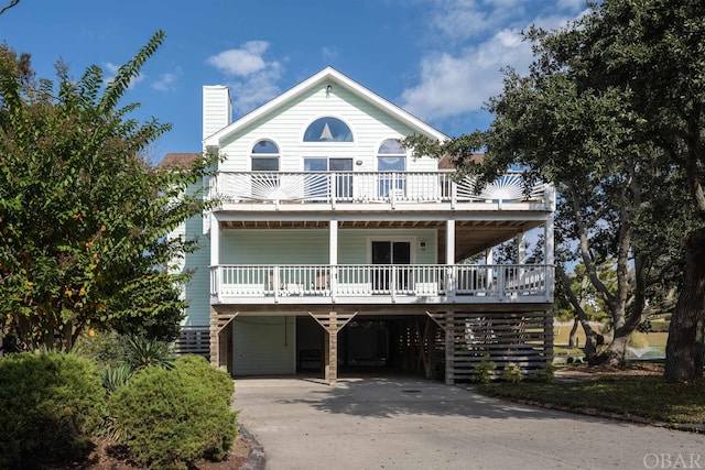 beach home with a porch, a balcony, driveway, a carport, and a chimney