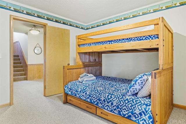 carpeted bedroom featuring a wainscoted wall, wooden walls, and a textured ceiling