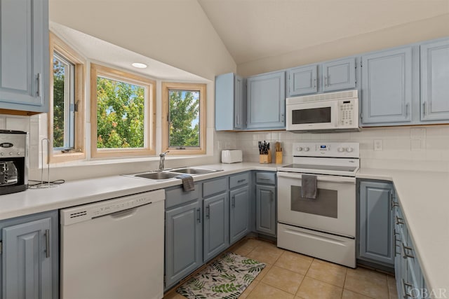 kitchen featuring white appliances, decorative backsplash, lofted ceiling, light countertops, and a sink