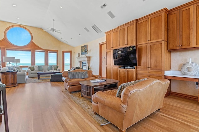 living area featuring a water view, a fireplace, visible vents, a ceiling fan, and light wood-type flooring