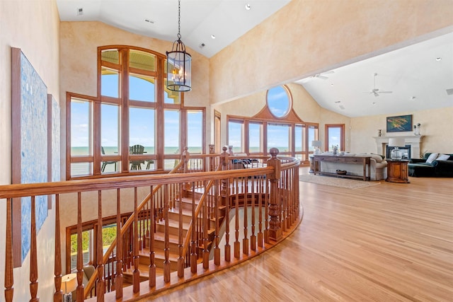 interior space with a notable chandelier, a water view, light wood-style floors, an upstairs landing, and high vaulted ceiling