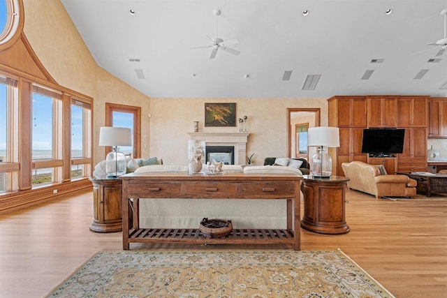 living room with light wood-type flooring, visible vents, a ceiling fan, and a glass covered fireplace