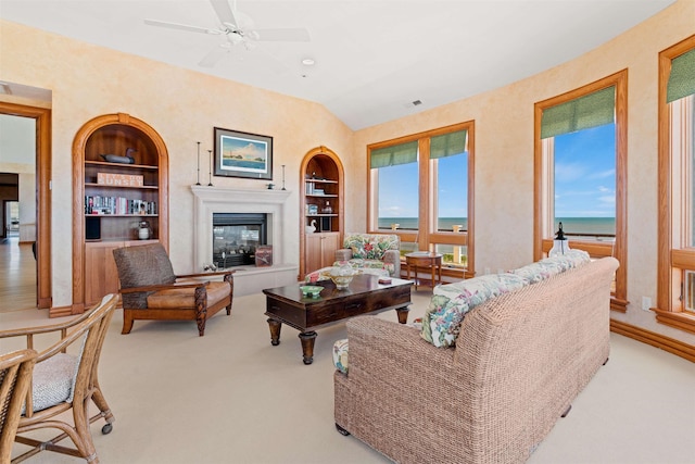 living area featuring light carpet, built in shelves, vaulted ceiling, and a glass covered fireplace