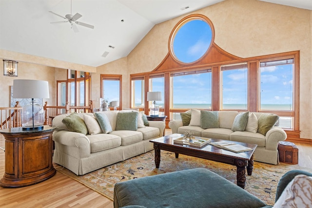 living area with visible vents, a ceiling fan, wood finished floors, a water view, and high vaulted ceiling