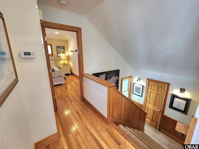 hall with lofted ceiling, an upstairs landing, and light wood-style flooring