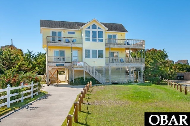 exterior space featuring fence, a balcony, roof with shingles, a lawn, and stairway