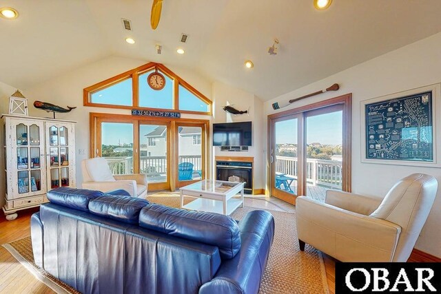 living area with light wood-style flooring, visible vents, a glass covered fireplace, recessed lighting, and vaulted ceiling