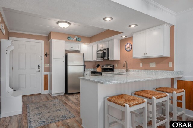 8123 S Old Oregon Inlet Rd Unit 208, Nags Head, NC 27959 - kitchen with stainless steel appliances, a peninsula, crown molding, white cabinetry, and a kitchen breakfast bar