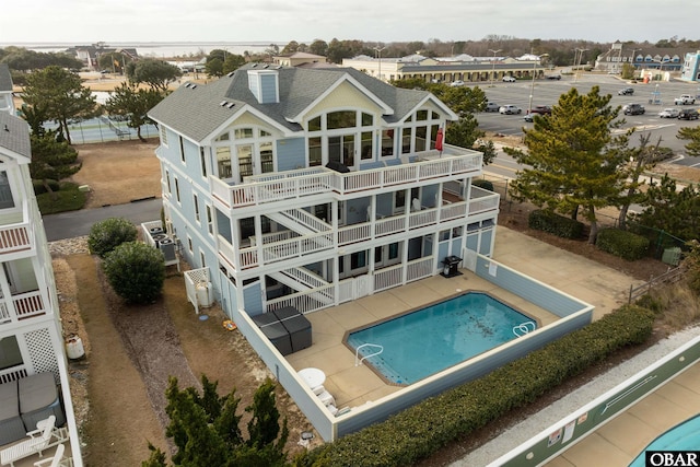 rear view of property featuring a shingled roof, a fenced in pool, a balcony, stairs, and a patio area