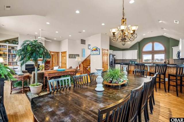 dining area with lofted ceiling, light wood finished floors, stairway, and a chandelier