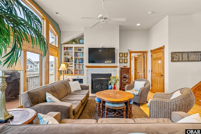 living room with built in shelves, a premium fireplace, wood finished floors, visible vents, and a ceiling fan