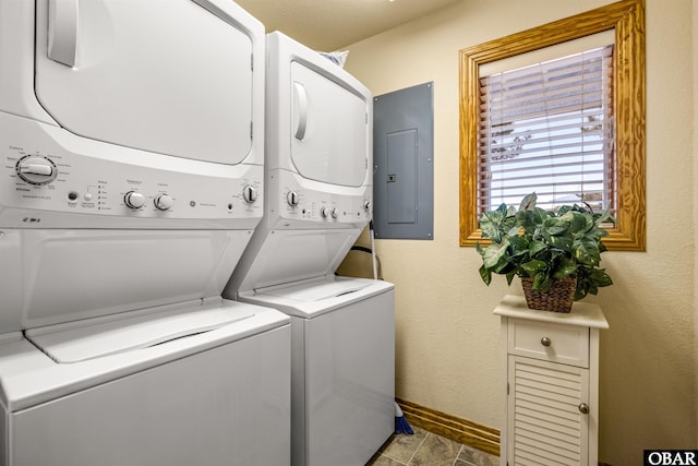 clothes washing area with stacked washer and dryer, laundry area, electric panel, baseboards, and a textured wall