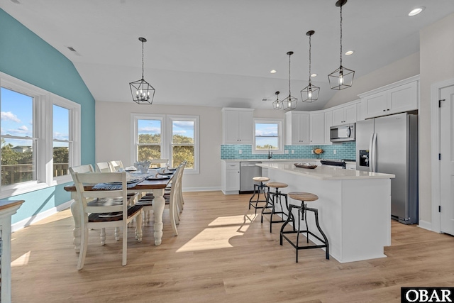 kitchen featuring a kitchen island, stainless steel appliances, decorative backsplash, vaulted ceiling, and white cabinetry