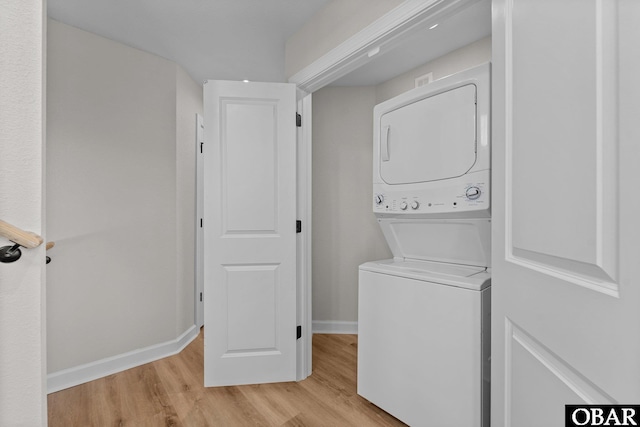 washroom featuring laundry area, baseboards, light wood finished floors, and stacked washing maching and dryer