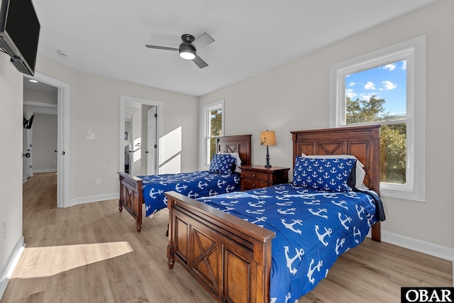 bedroom with multiple windows, light wood-style floors, and baseboards