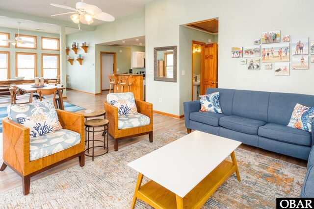 living room with baseboards, ceiling fan, a towering ceiling, and light wood finished floors