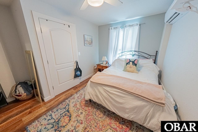 bedroom featuring a wall mounted air conditioner, wood finished floors, a ceiling fan, and baseboards