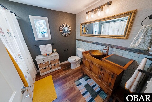 bathroom featuring wood finished floors, toilet, vanity, and a textured wall