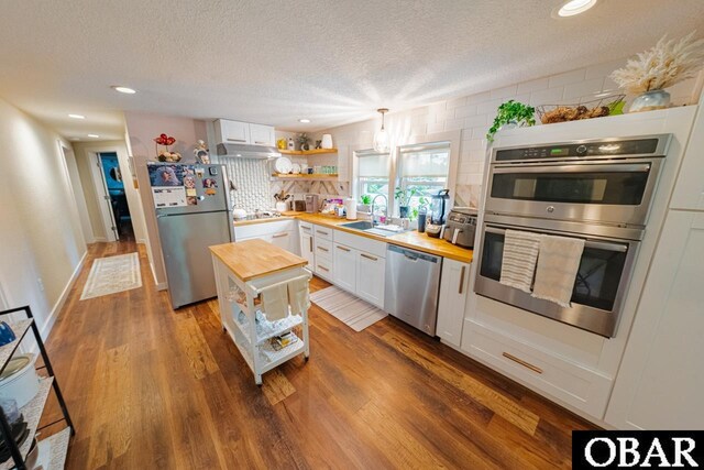 kitchen with appliances with stainless steel finishes, wood counters, a sink, white cabinets, and a textured ceiling