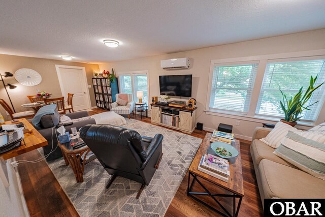 living area with an AC wall unit, wood finished floors, baseboards, and a textured ceiling
