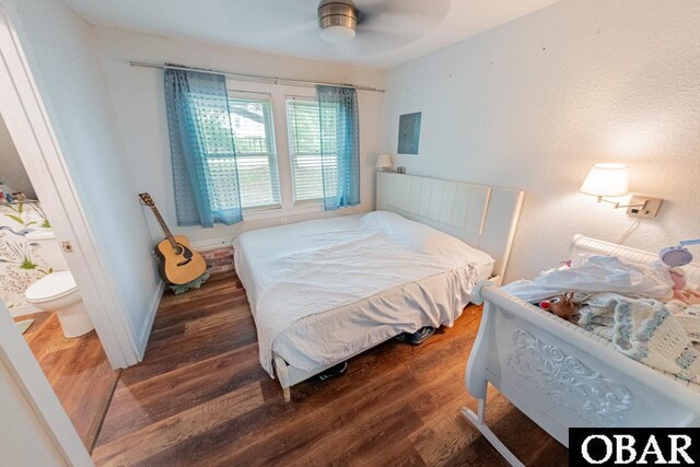 bedroom featuring wood finished floors, electric panel, and ensuite bathroom