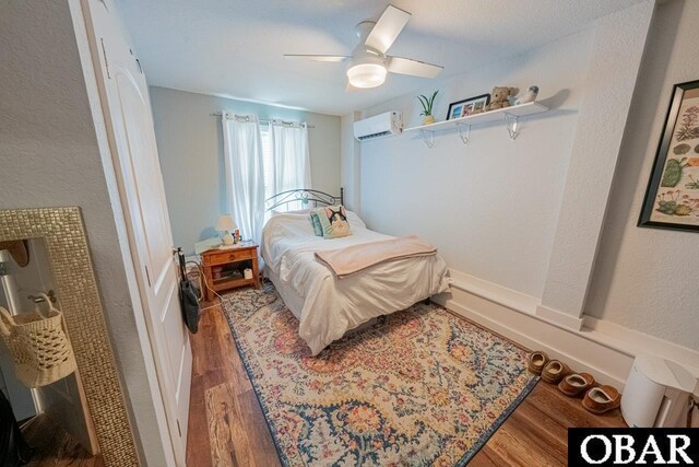 bedroom with a wall mounted AC, wood finished floors, ceiling fan, and a textured wall