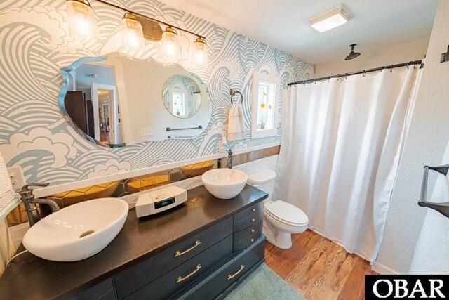 full bath featuring wallpapered walls, wood finished floors, toilet, double vanity, and a shower with shower curtain