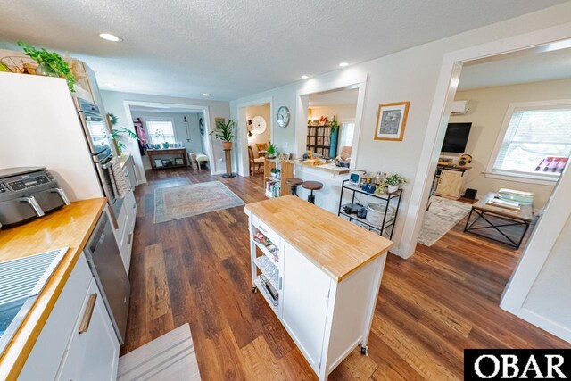 kitchen with butcher block countertops, healthy amount of natural light, dark wood finished floors, a textured ceiling, and recessed lighting