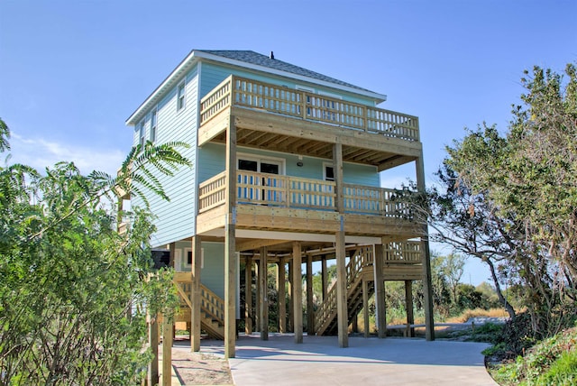 raised beach house featuring a carport, driveway, stairway, and a shingled roof