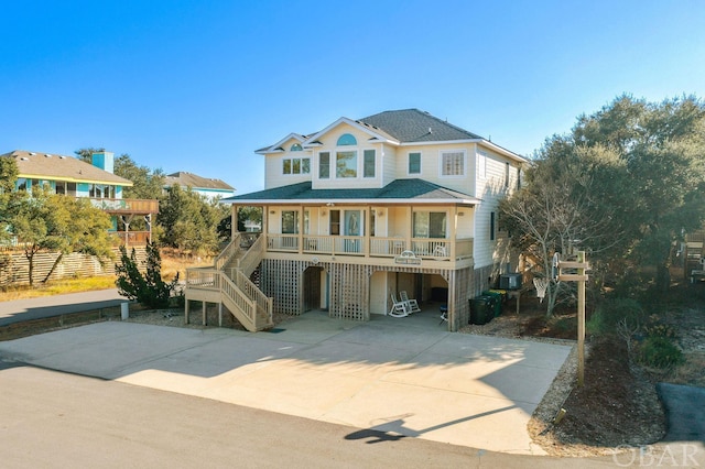 beach home with a porch, a shingled roof, concrete driveway, a carport, and stairs