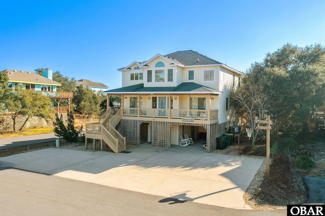 raised beach house featuring stairs, covered porch, and a shingled roof