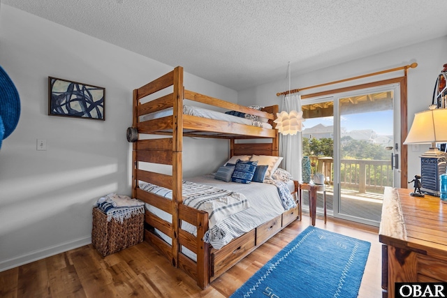 bedroom featuring a textured ceiling, baseboards, wood finished floors, and access to exterior