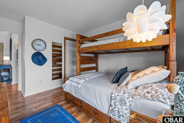 bedroom with baseboards, a textured ceiling, wood finished floors, and a closet