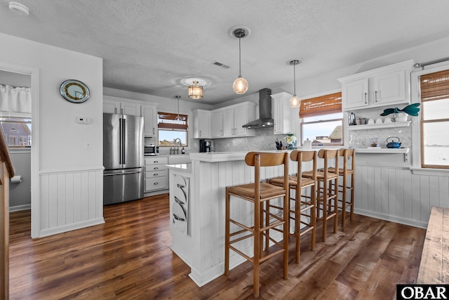 kitchen featuring a breakfast bar area, a textured ceiling, dark wood finished floors, freestanding refrigerator, and wall chimney exhaust hood