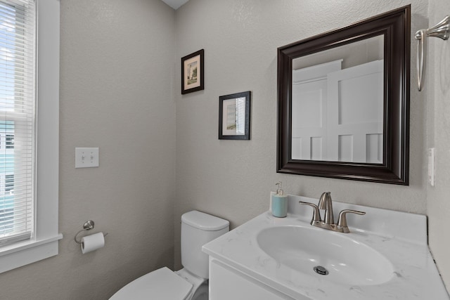 half bath with a textured wall, vanity, and toilet