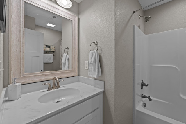 bathroom featuring vanity, tub / shower combination, and a textured wall