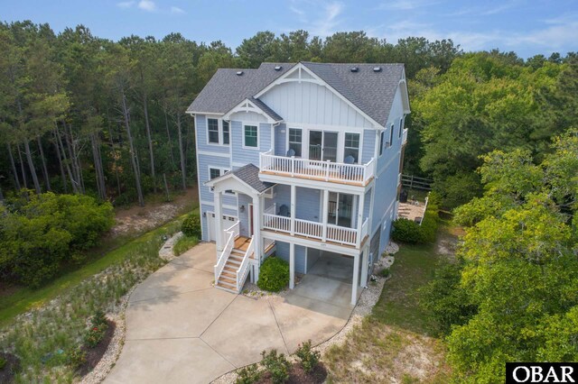 view of front of property featuring driveway, covered porch, board and batten siding, a shingled roof, and a balcony