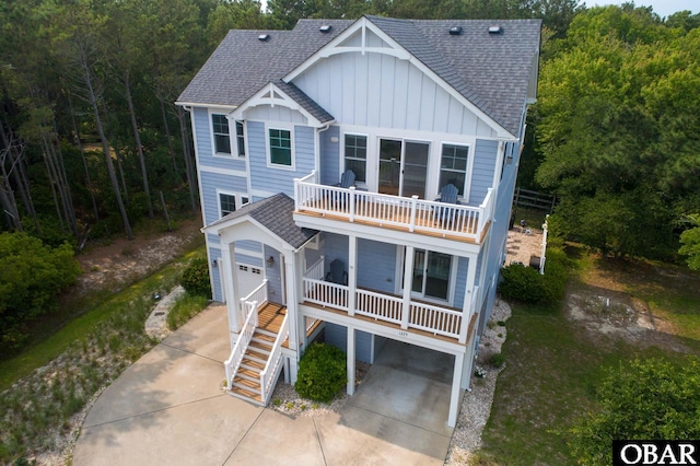 coastal inspired home with a porch, board and batten siding, concrete driveway, a shingled roof, and stairs