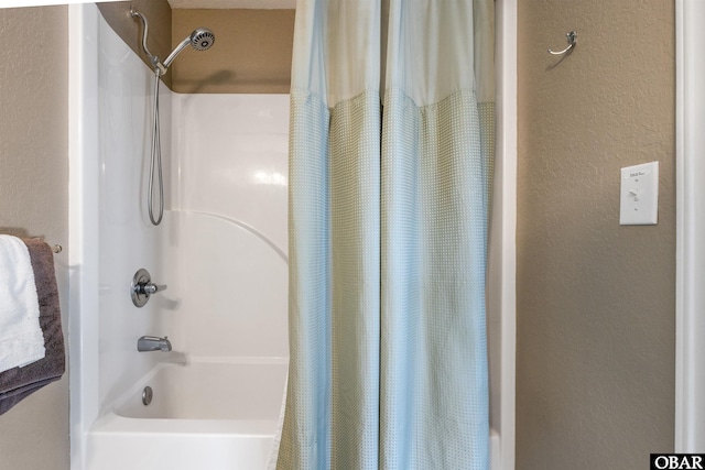 full bathroom with a textured wall and shower / bathtub combination with curtain