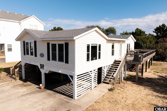 view of front facade featuring a shingled roof, stairway, a carport, and concrete driveway